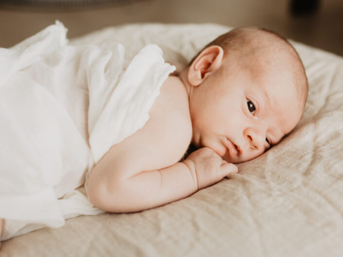 Ein Neugeborenes was eingewickelt in Tüchern auf einer Decke liegt
