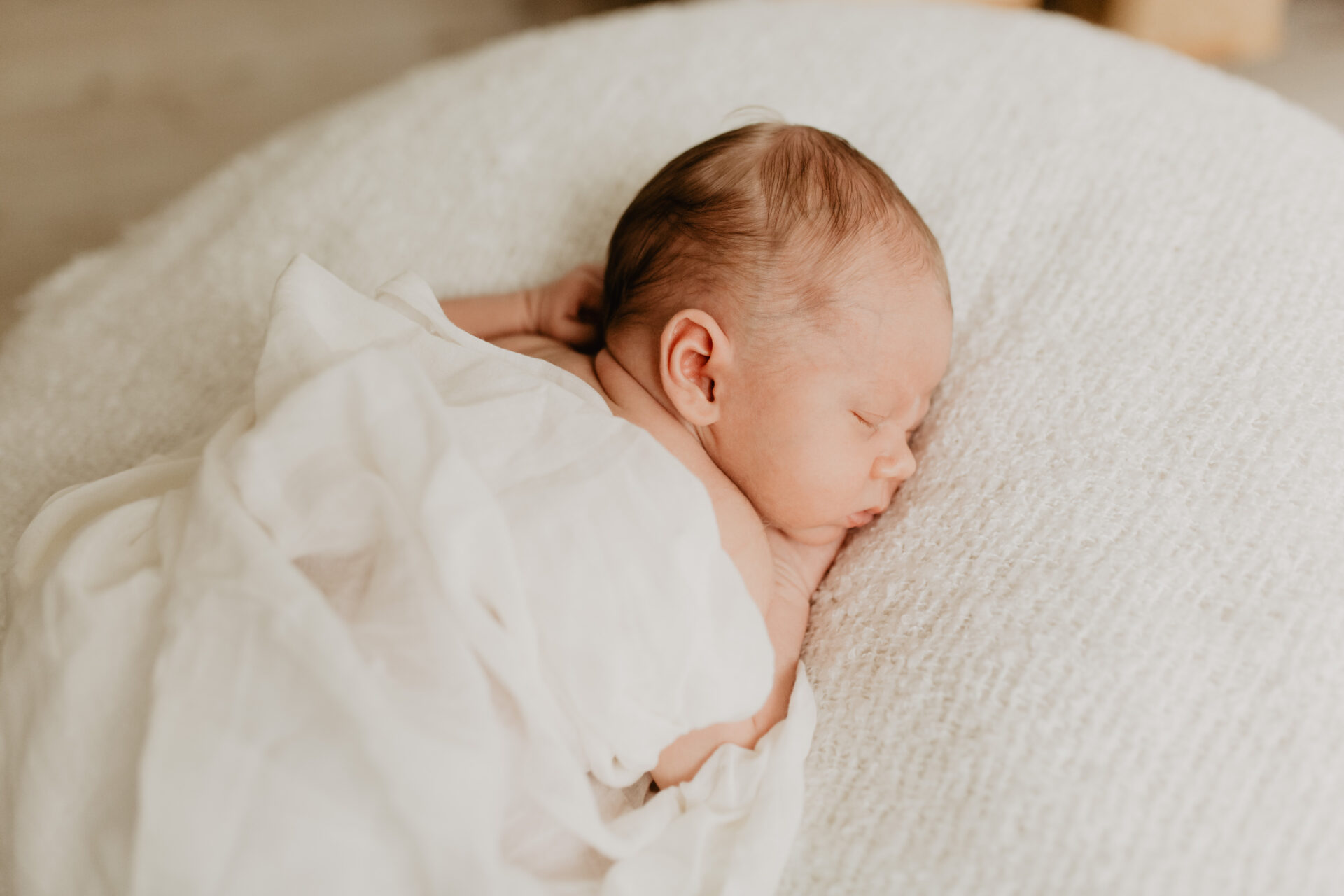 Ein Baby liegt während einem Newbornshooting auf dem Bauch, die Augen geschlossen.