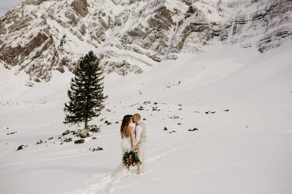 Ein Brautpaar im Winter, was sich vor einer Bergkulisse küsst